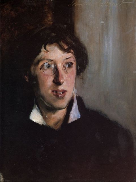 Painting. Shown from the chest up, a person with dark hair, pale skin, and a narrow, oval face looks off to our right. Round spectacles perch on the nose, and red lips are parted. A bright white collar stands out from under their black top. The background is painted loosely with bronze-brown to our left and pearl-white to our right.